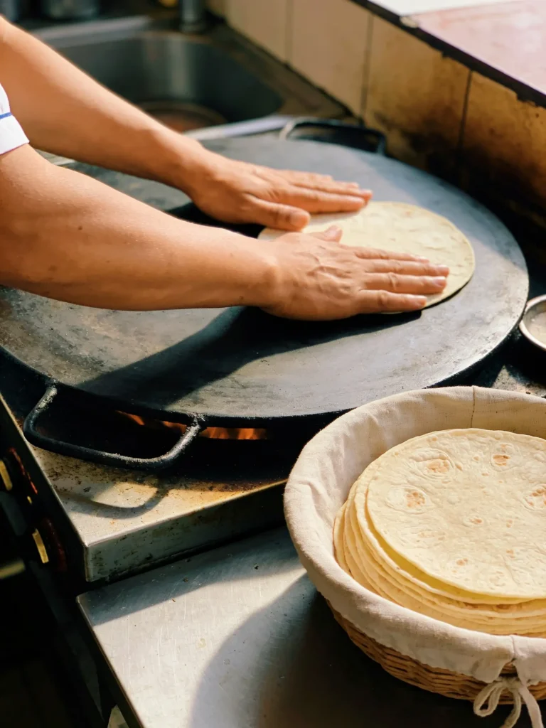 Hands cooking fresh flour tortillas on a comal